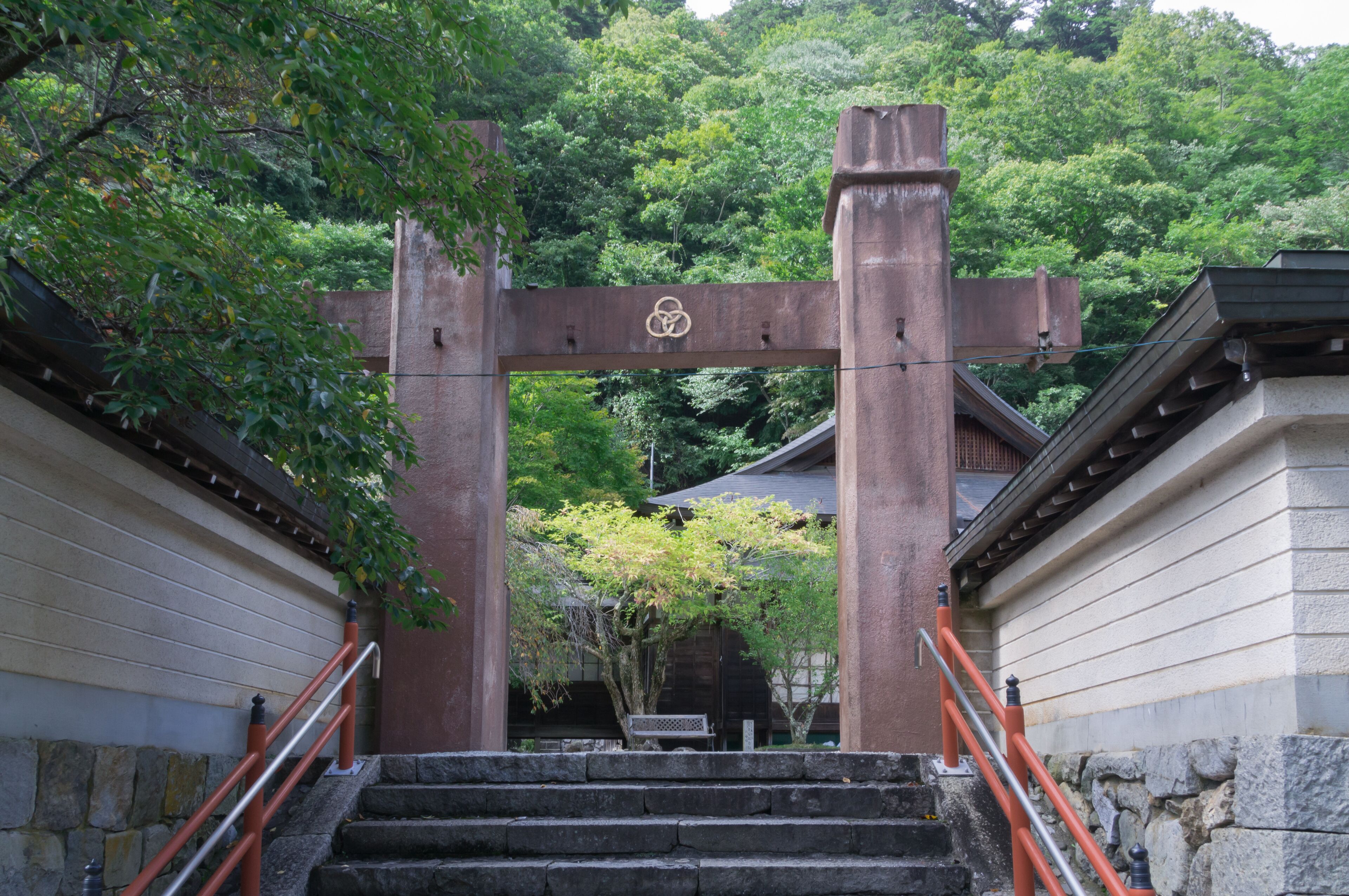 A traditional Japanese torii gate at the entrance of a temple, surrounded by lush greenery.