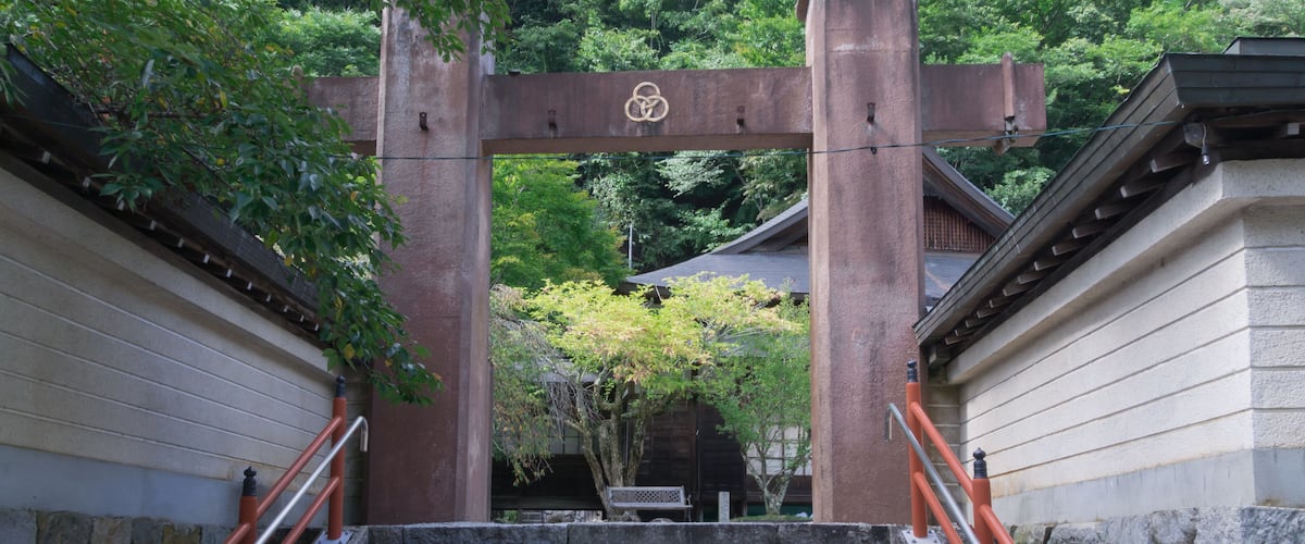A traditional Japanese torii gate at the entrance of a temple, surrounded by lush greenery.