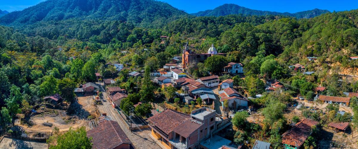 A mountainous village with terraced houses, a church, and lush greenery.