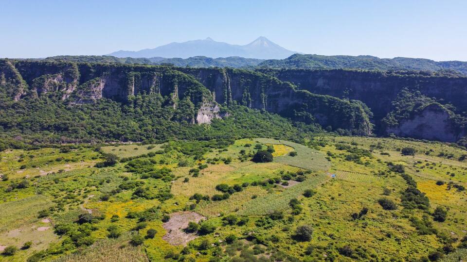 A mountainous landscape with a prominent volcano in the background and terraced fields in the foreground.
