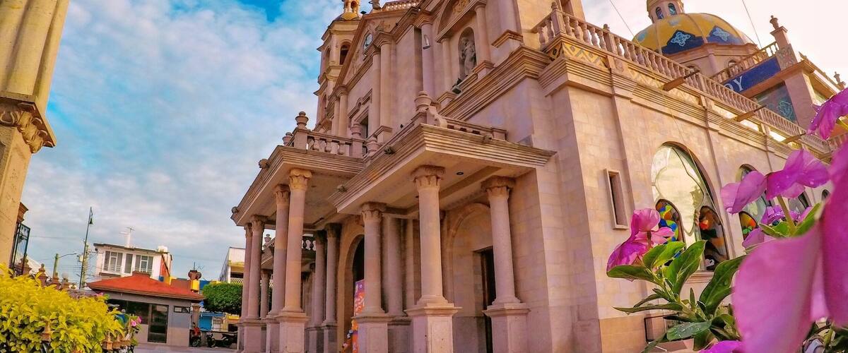 A historic church with a bell tower and dome, surrounded by a plaza with flowers and a statue.