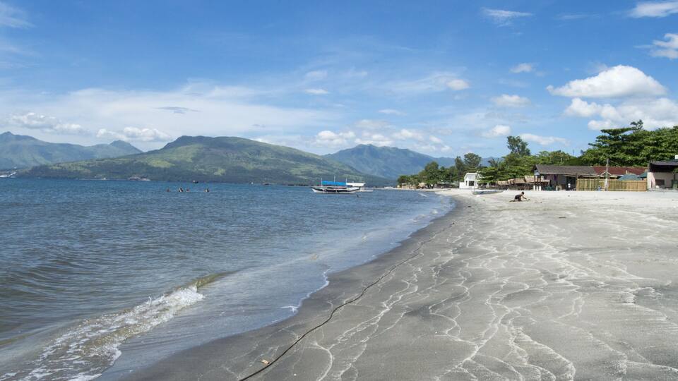 A beach with a boat, mountains, and a clear sky.