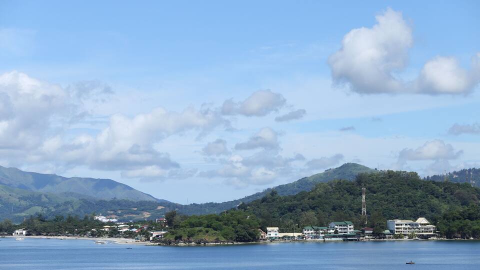A coastal town with buildings, a clear sky, and mountains in the background.