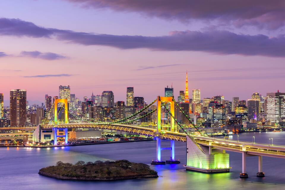 A brightly lit bridge with a city skyline in the background.