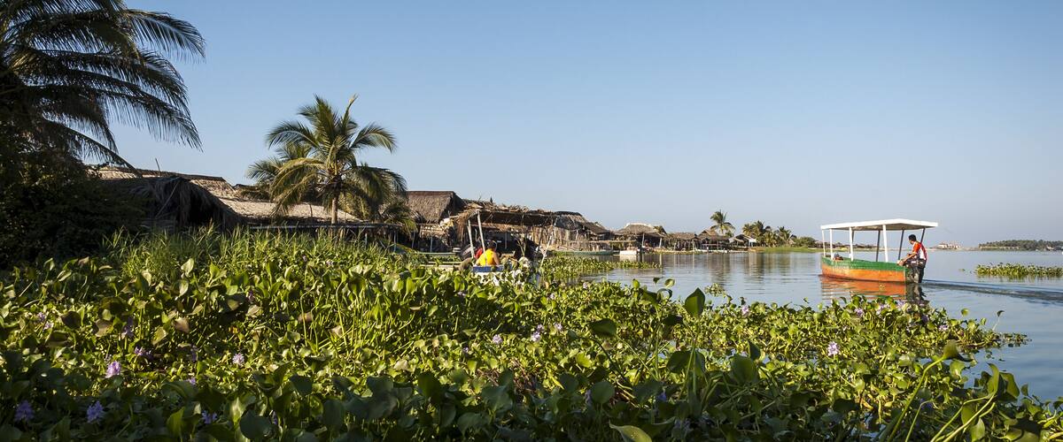 A calm lake with a boat, lush greenery, and traditional huts.