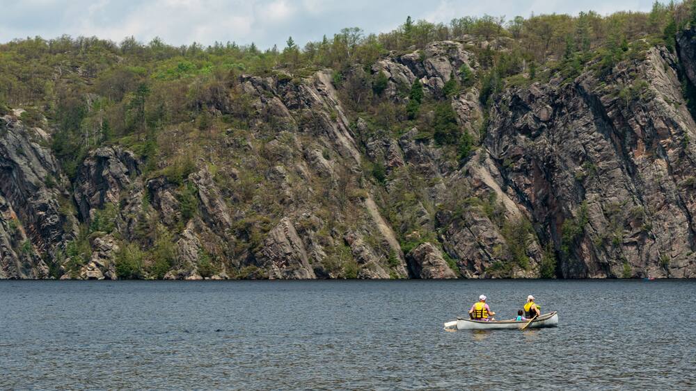 A calm lake with rocky cliffs in the background and a small boat with two people paddling.