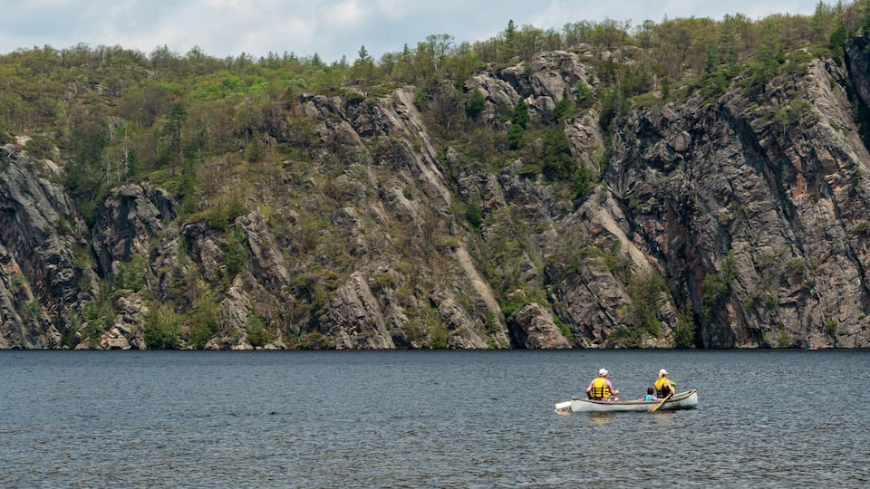 A calm lake with rocky cliffs in the background and a small boat with two people paddling.