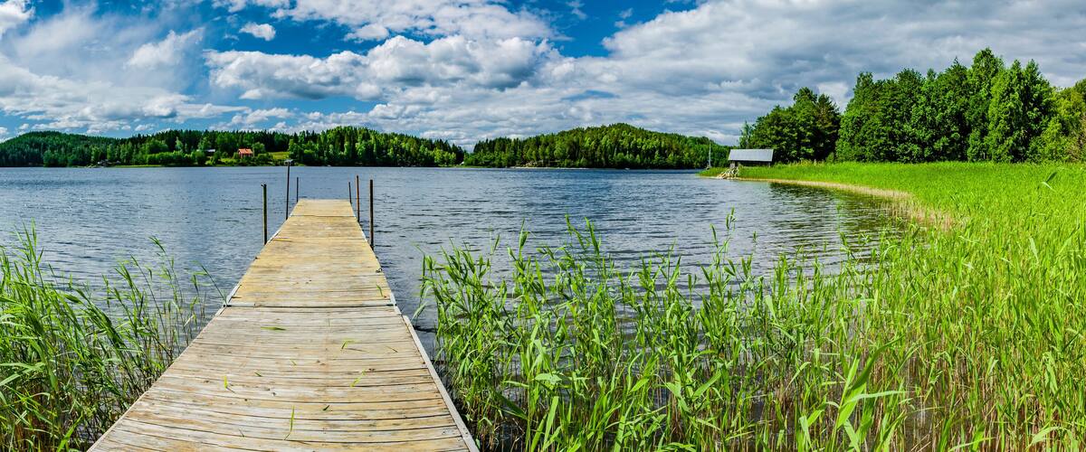 A wooden dock extending into a calm lake surrounded by lush greenery and forested hills.