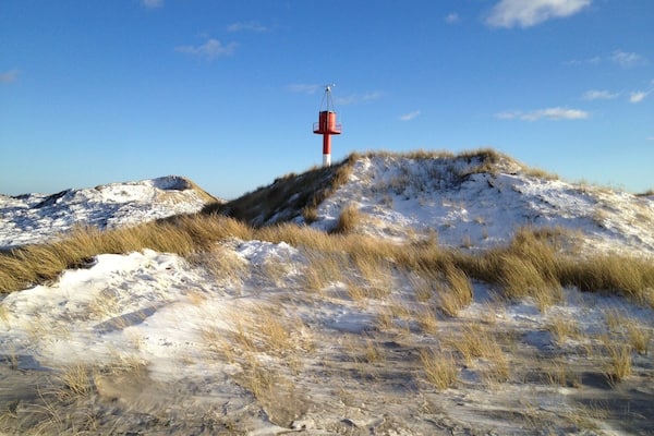 Un paysage de dunes enneigées, avec un phare rouge et blanc perché sur une colline.
