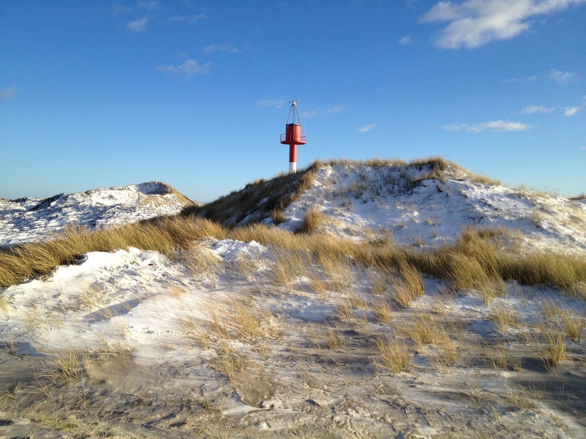 A snow-covered dune landscape with a red and white beacon on a hill.