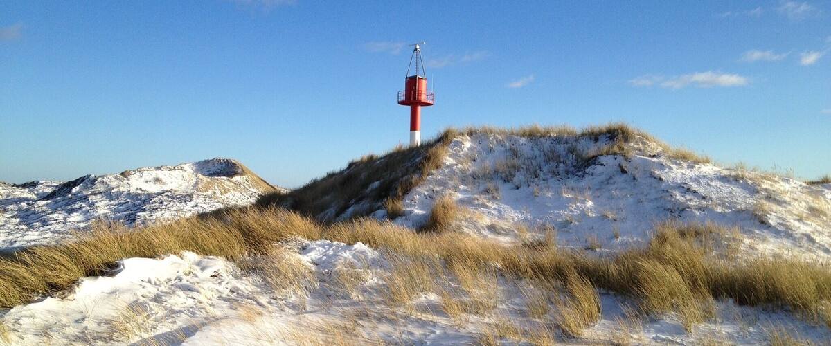 A snow-covered dune landscape with a red and white beacon on a hill.