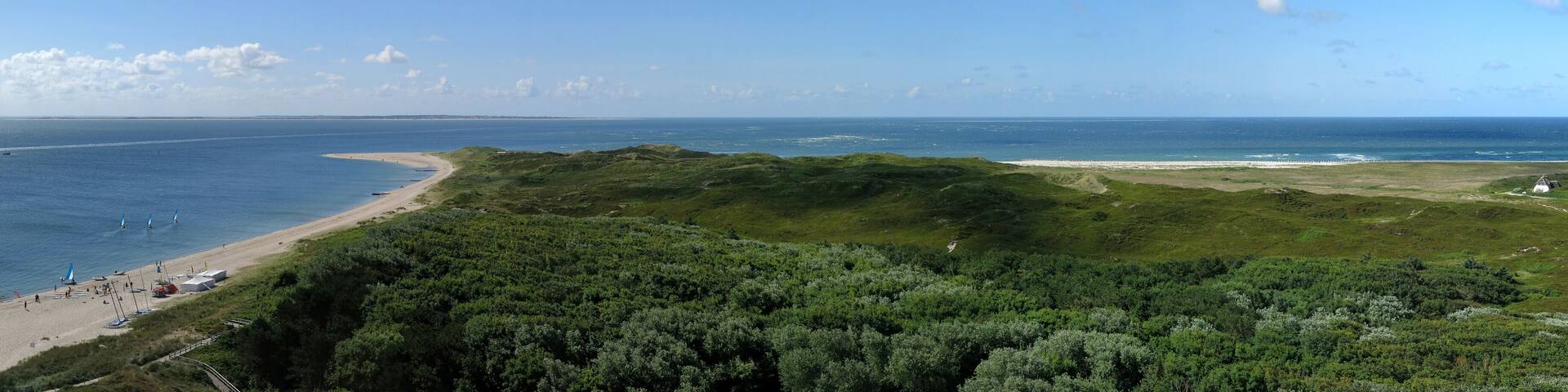 A coastal landscape with a sandy beach, a grassy hill, and the ocean.