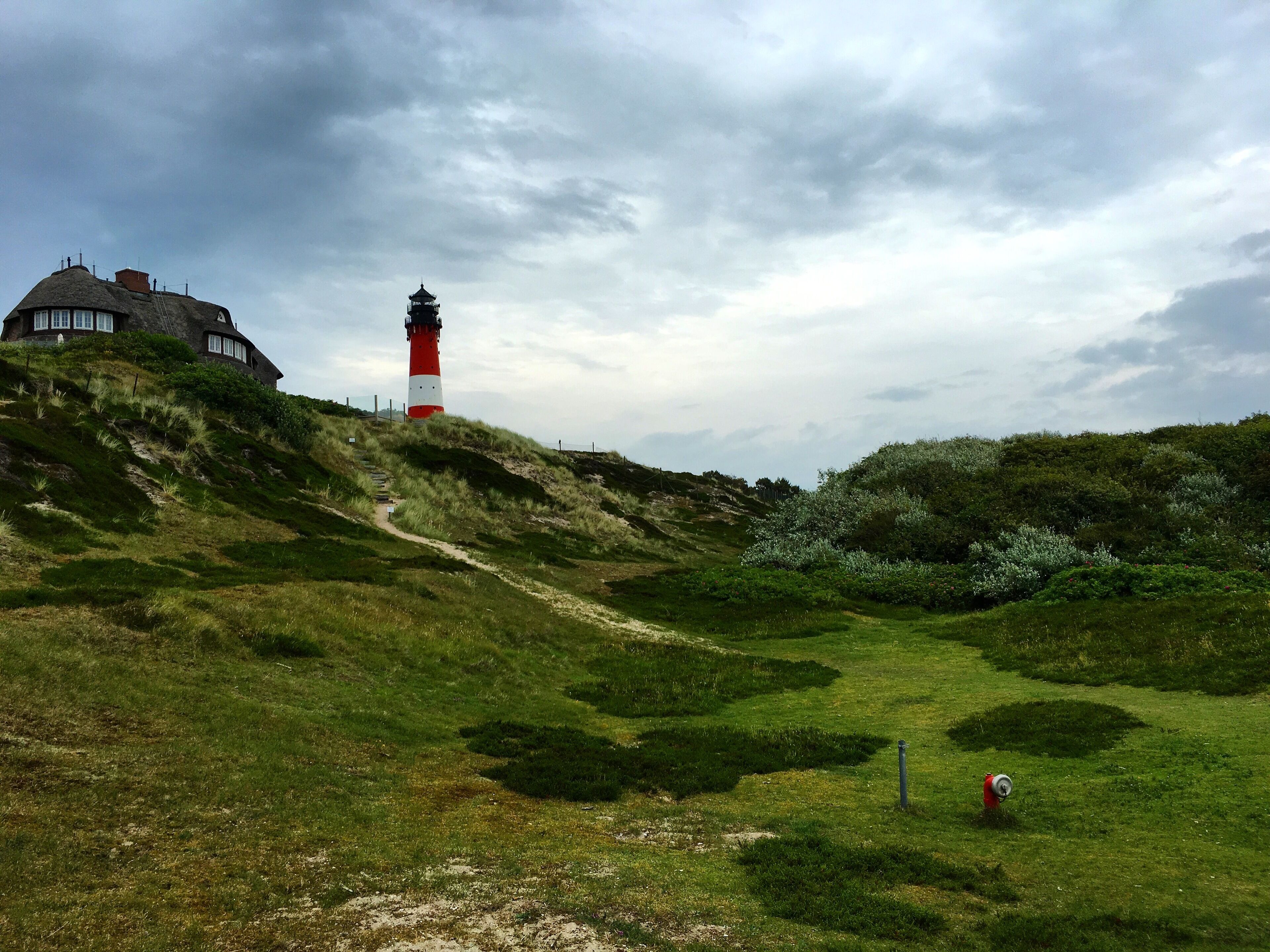 A lighthouse on a grassy hill with a building in the background.