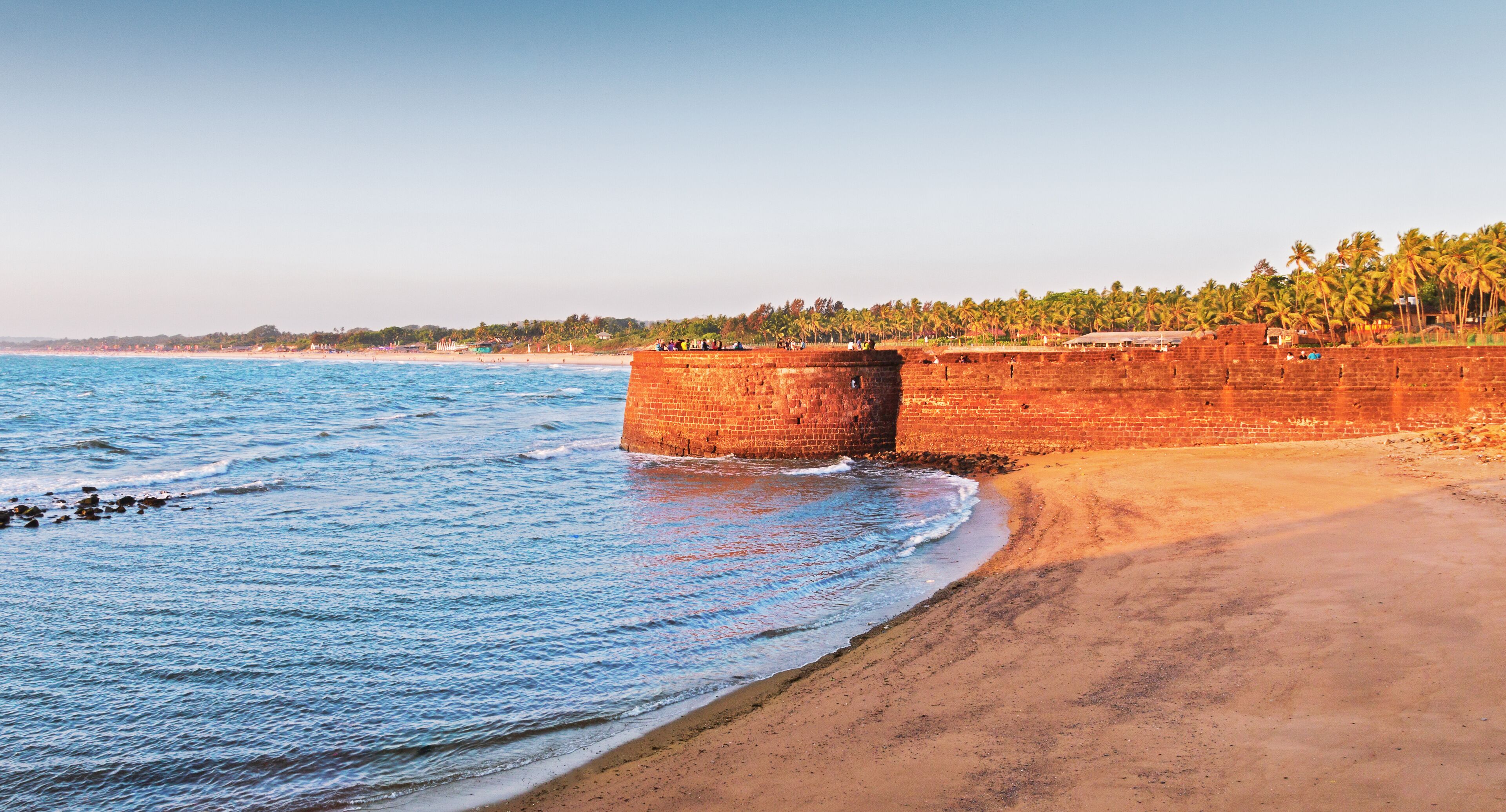 A beach with a large brick wall and palm trees in the background.