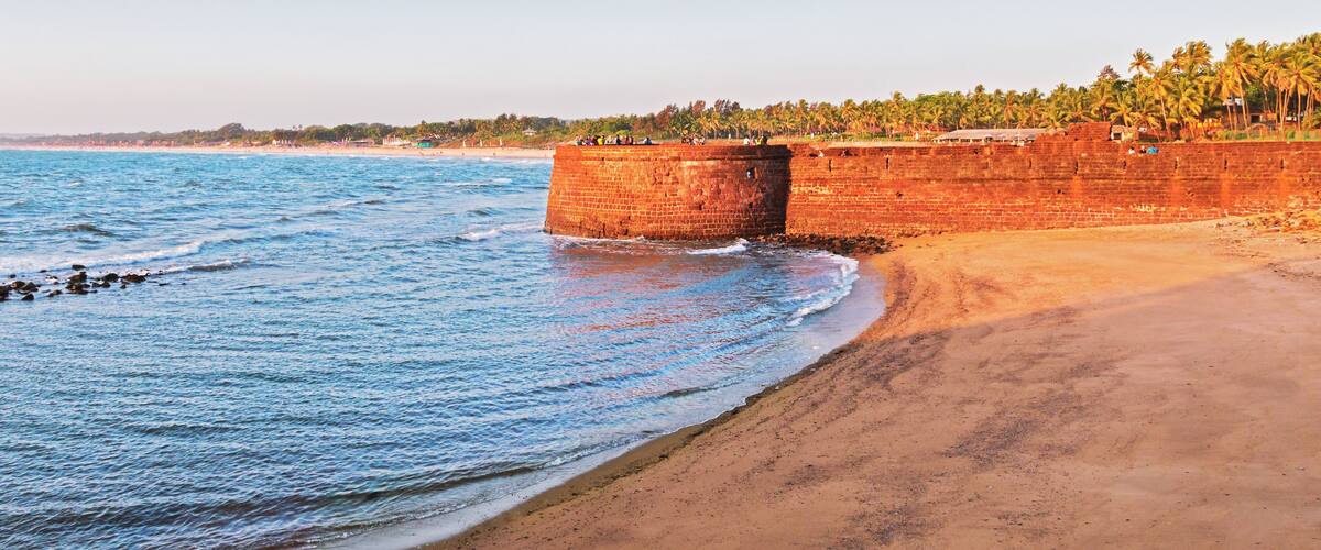 A beach with a large brick wall and palm trees in the background.