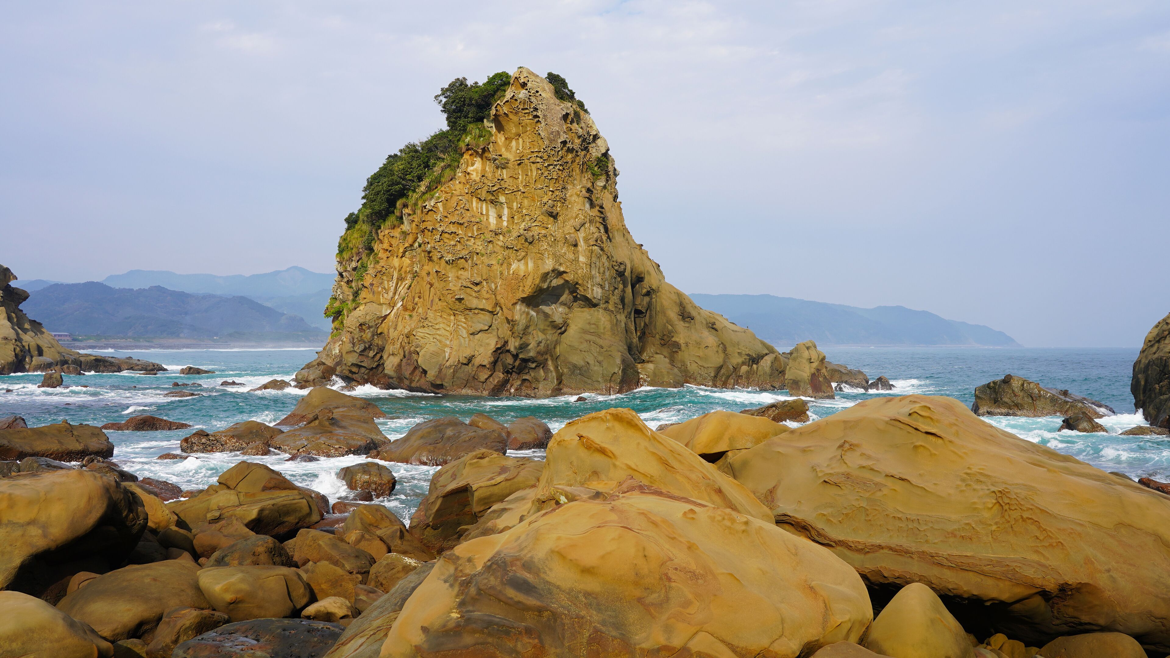 Volcanic mountains overgrown with plants and trees by the shore of the Pacific Ocean. Clear bright sea water, stone beach, mountain in the ocean.
