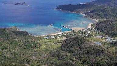 A coastal landscape with a beach, clear blue waters, and lush green hills.