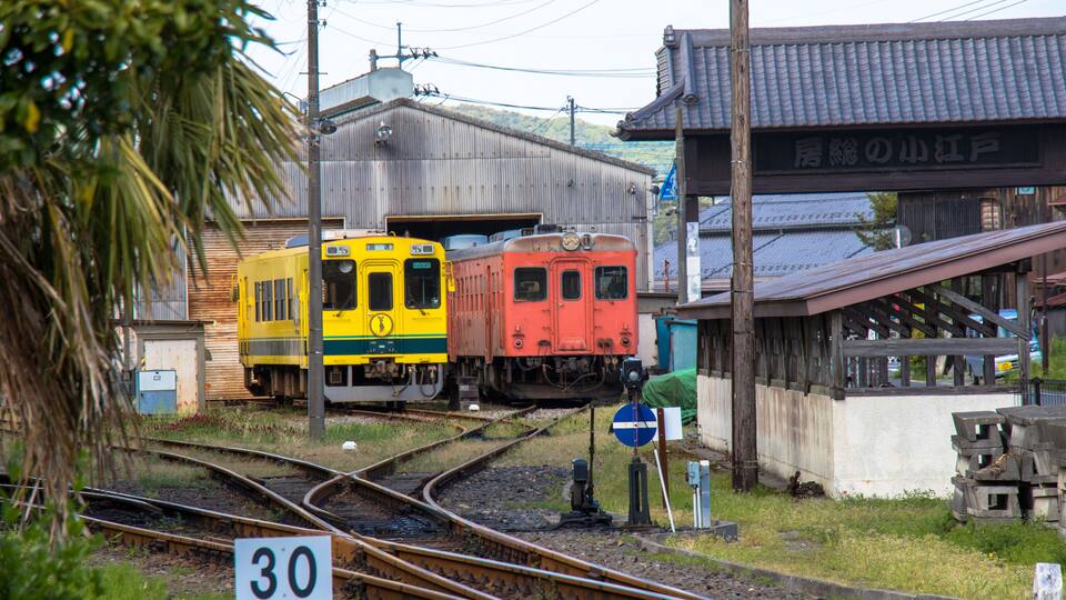 A railway junction with two trains, a speed limit sign, and a traditional building.