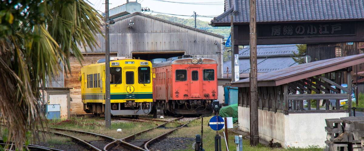 A railway junction with two trains, a speed limit sign, and a traditional building.