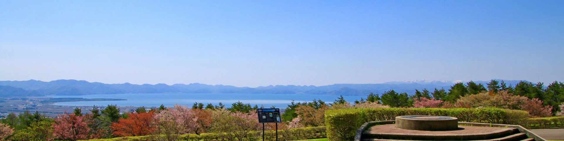 Um parque com uma plataforma de observação, uma placa e uma vista panorâmica de montanhas e um lago.