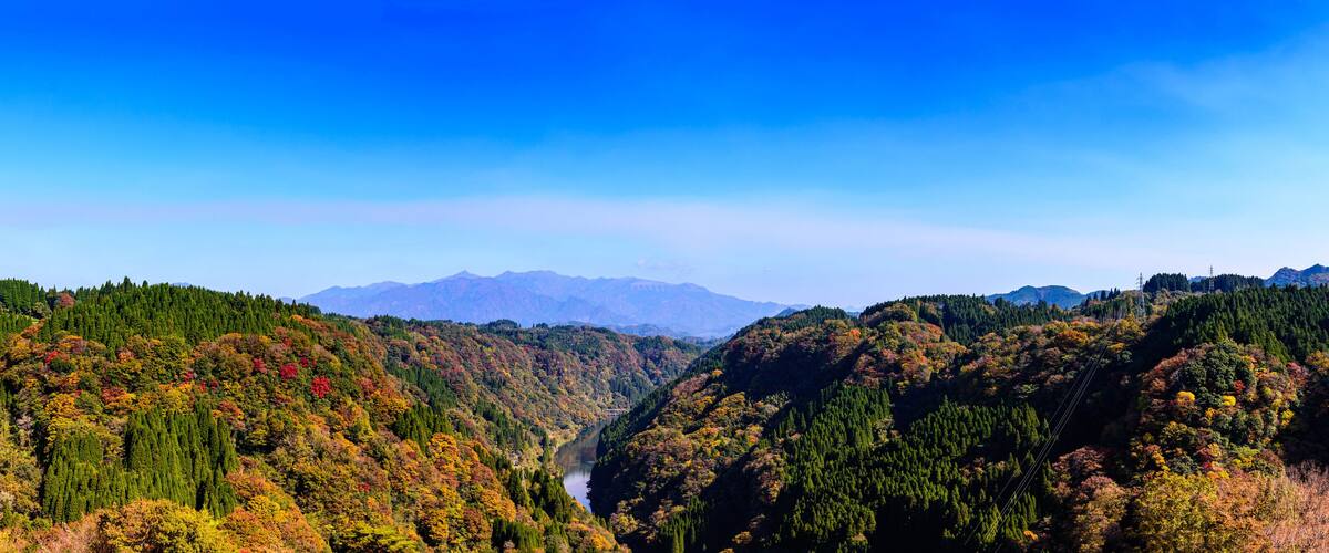 A valley with a river, surrounded by forested hills and distant mountains.