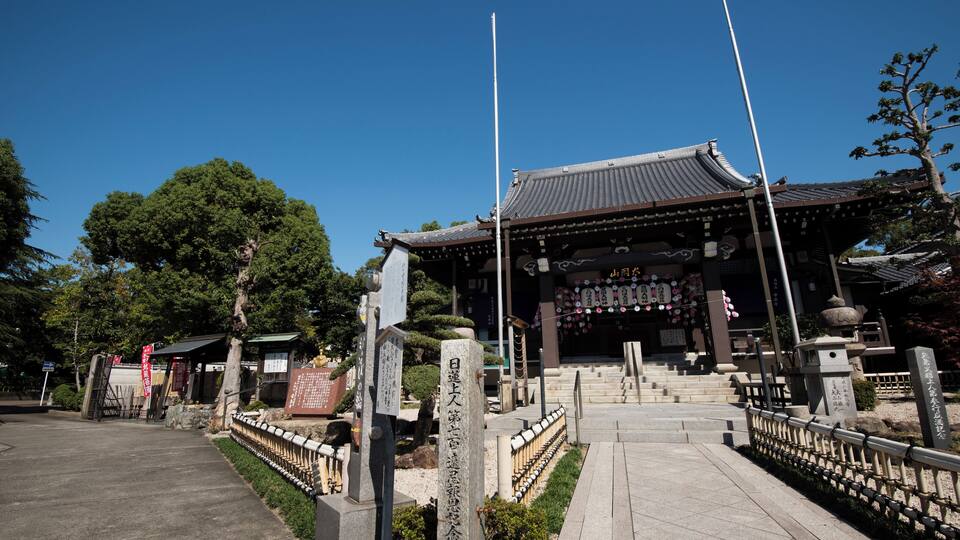Ein traditioneller japanischer Tempel mit Ziegeldach, Steinlaternen und einem Steinsockel mit Inschriften.