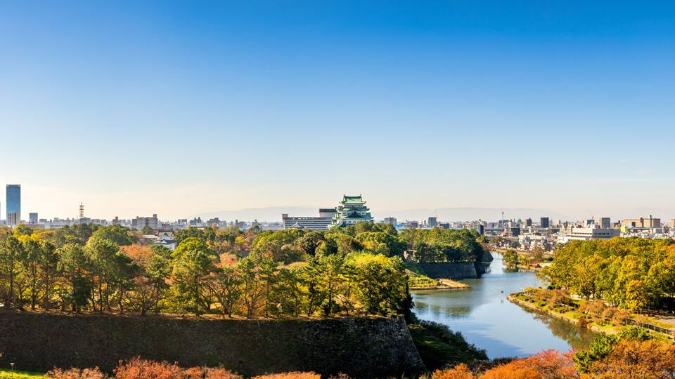 Eine Stadtlandschaft mit Herbstlaub, einem Fluss und einer traditionellen japanischen Burg.