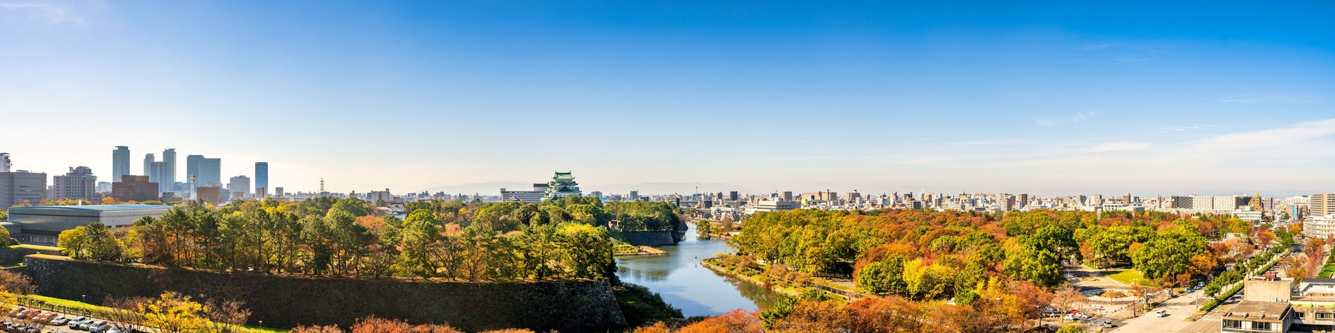 Paisagem urbana com folhagem outonal, um rio e um castelo japonês tradicional.
