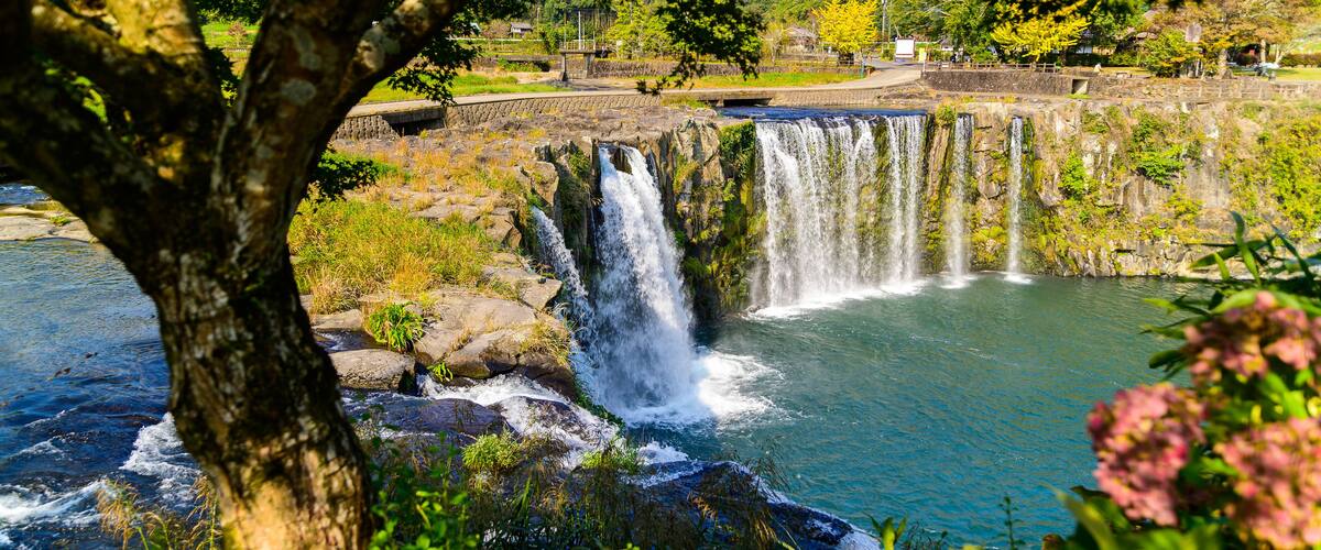 A waterfall cascading into a clear blue pool surrounded by lush greenery and trees.