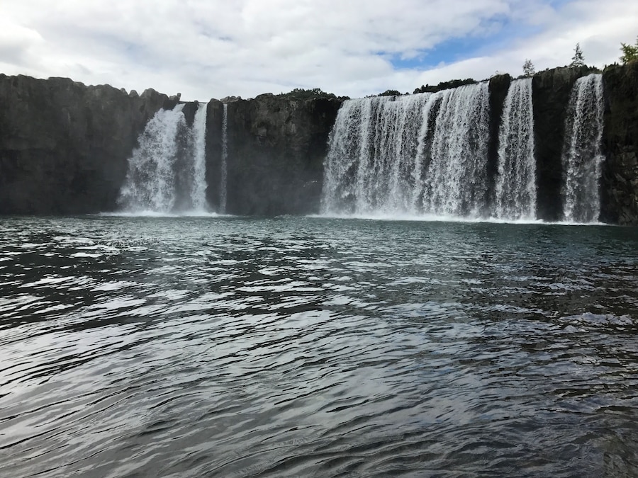 A large waterfall cascading into a body of water surrounded by rocky cliffs.