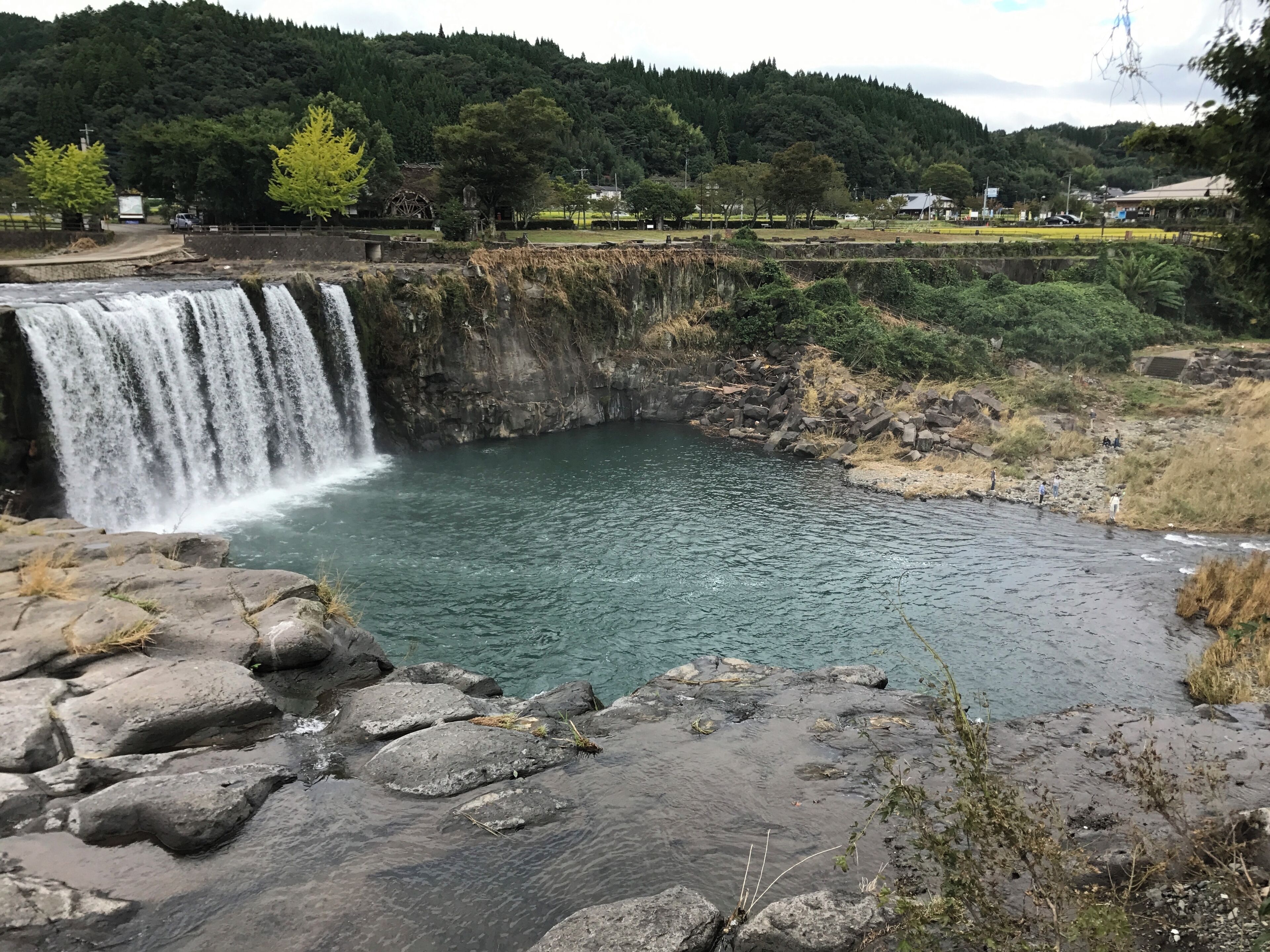 A waterfall cascading into a clear river surrounded by rocky terrain and lush greenery.