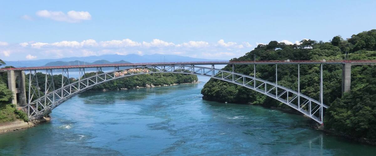 A steel bridge over a river with mountains in the background.