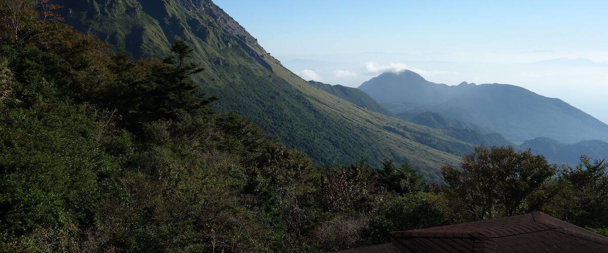 A mountain range with dense green forests and a clear blue sky.