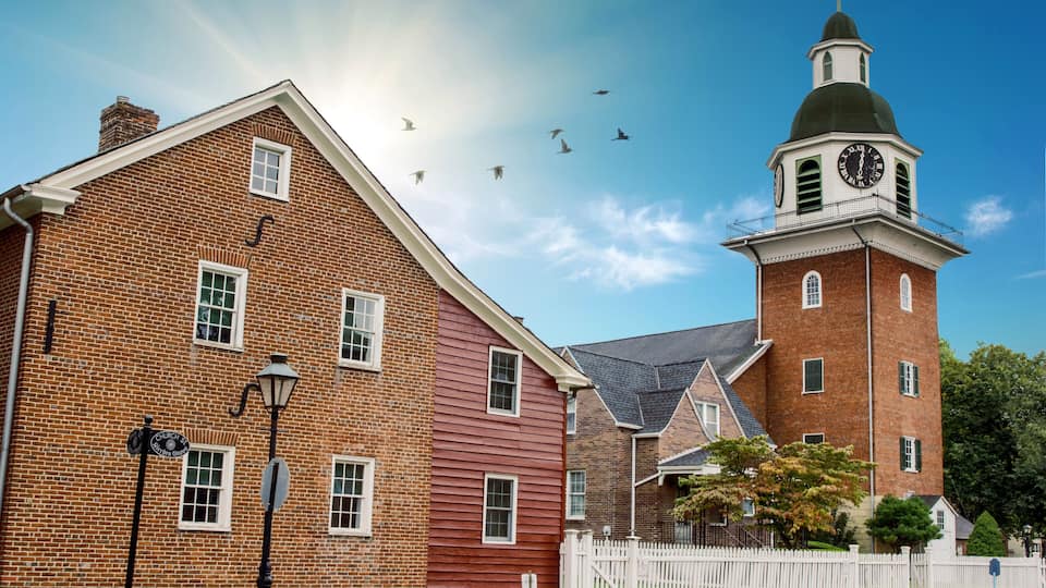 A brick building with a clock tower, a white picket fence, and a street lamp.