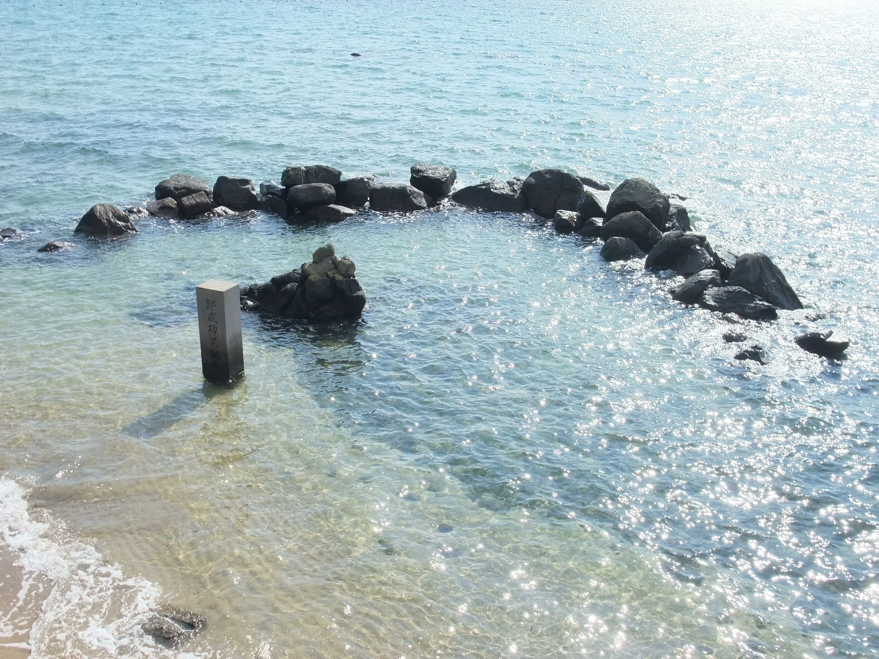 Una playa despejada con rocas y un poste de madera en el agua.