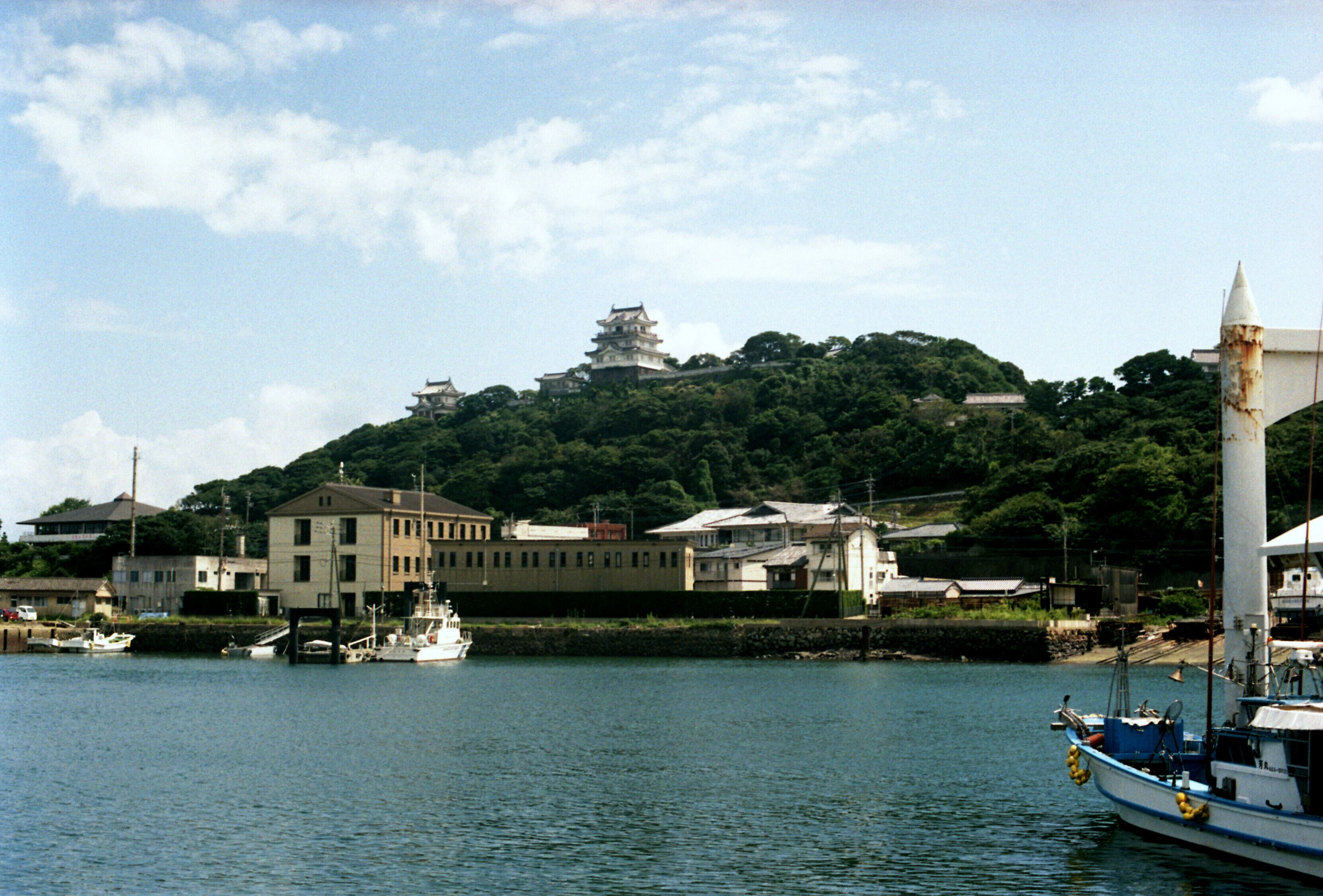A coastal town with a historic castle on a hill, boats docked at the harbor, and a lighthouse.