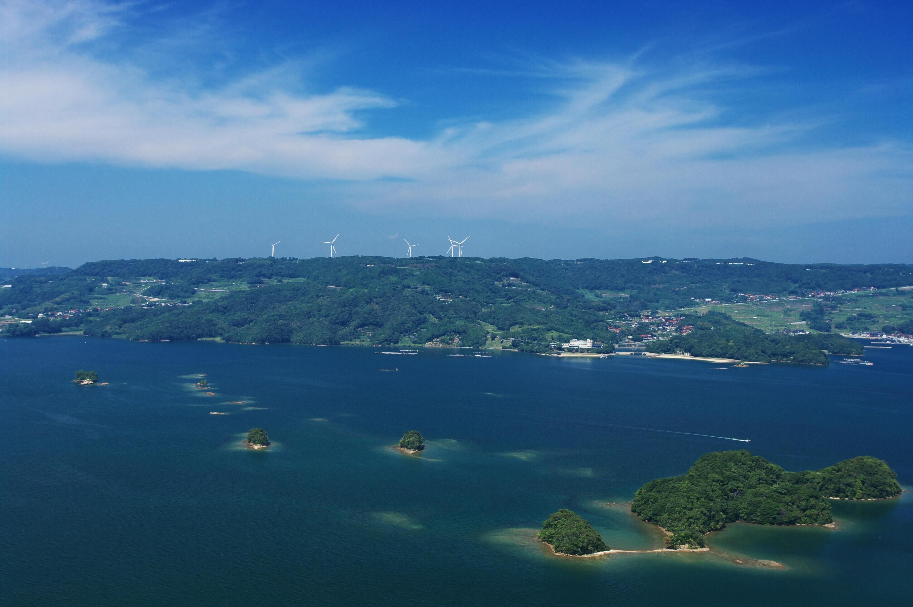 A coastal landscape with wind turbines, islands, and a clear sky.