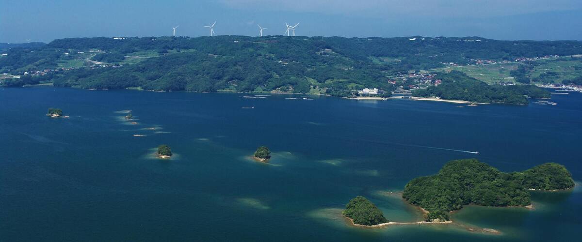 A coastal landscape with wind turbines, islands, and a clear sky.