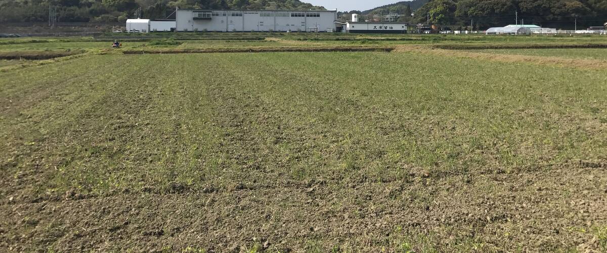A rural landscape with a large white building, fields, and hills in the background.