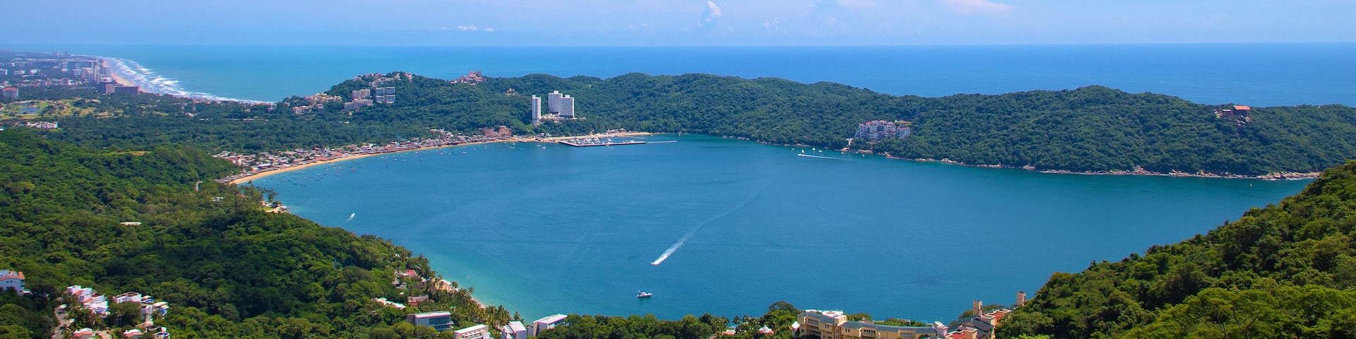 A coastal landscape with a bay, a beach, and a cityscape in the distance.