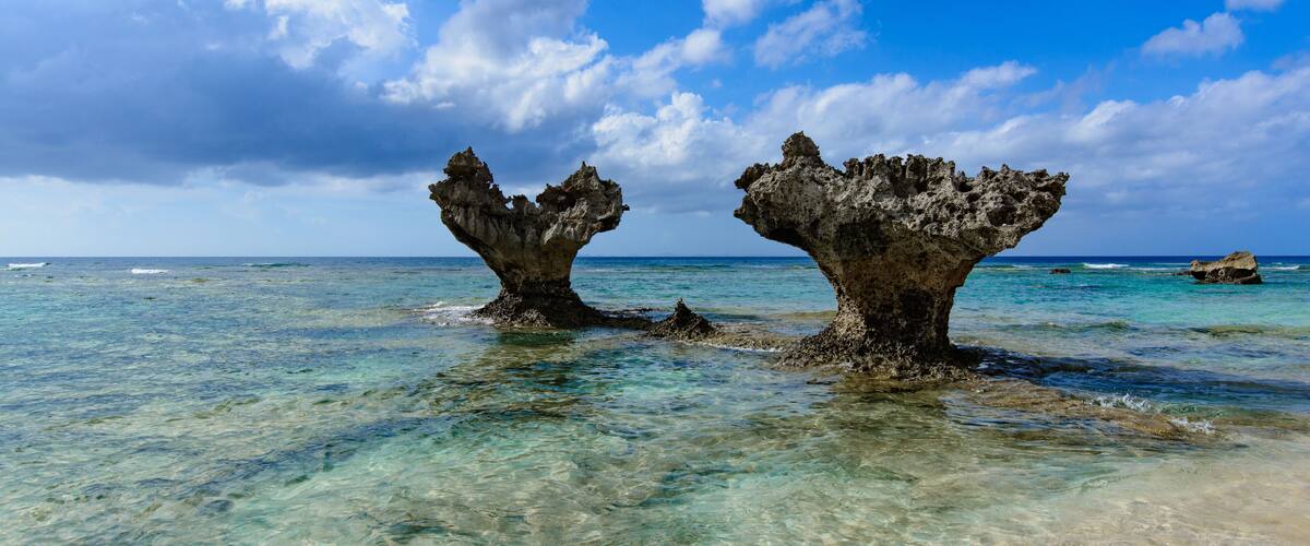 Clear blue water, two rock formations, and a partly cloudy sky.