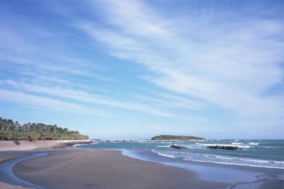 A beach with a curved shoreline, calm waves, and a distant island.