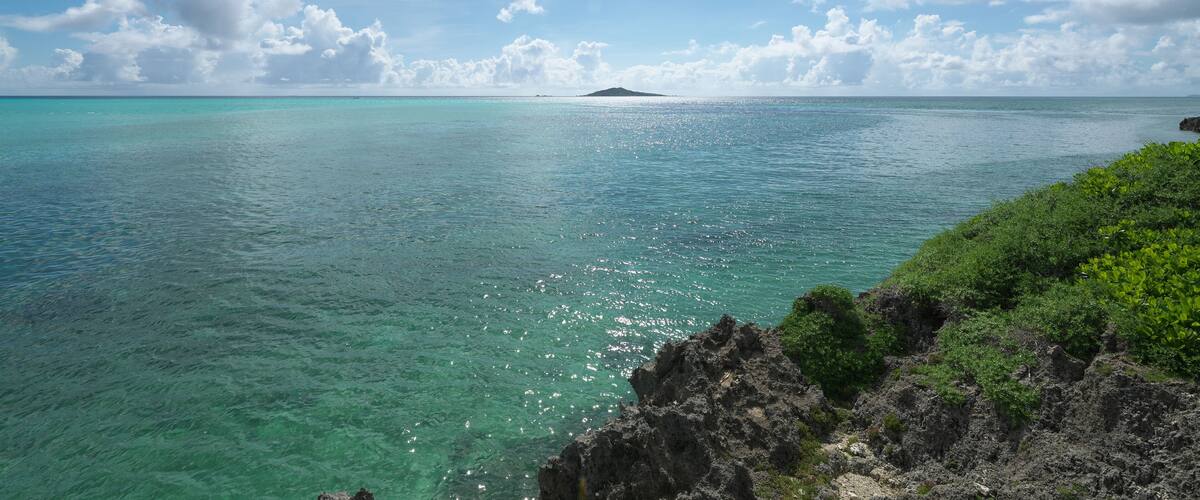 A clear blue sea with a rocky coastline and a small island in the distance.