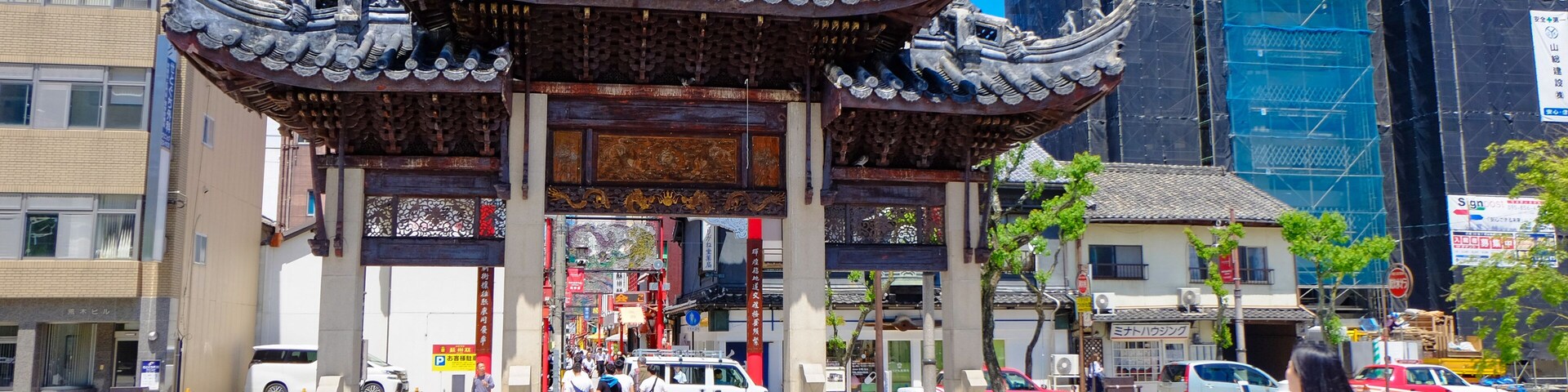Una puerta tradicional china con un diseño de techo ornamentado, un edificio moderno con andamios y un cielo azul despejado.