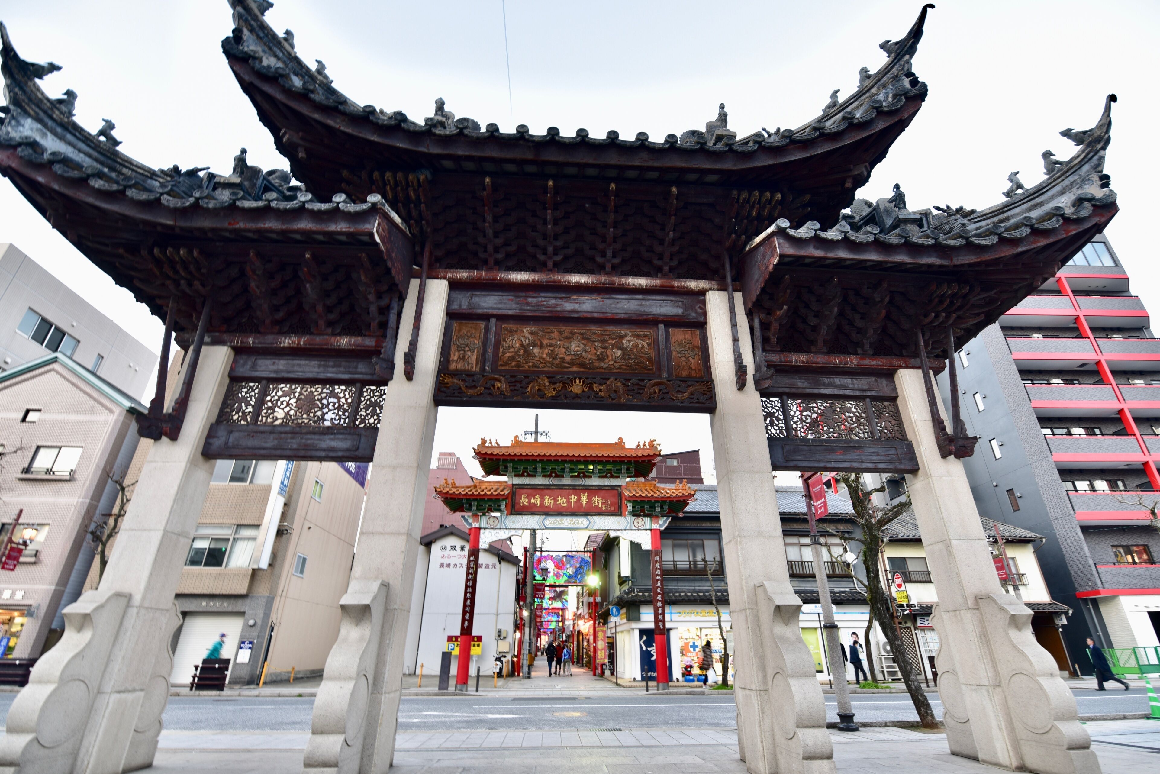 A traditional Chinese gate with ornate carvings and a red roof, leading to a modern building complex.