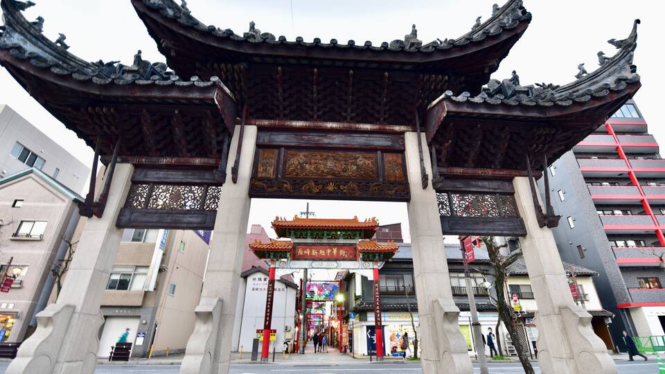 A traditional Chinese gate with ornate carvings and a red roof, leading to a modern building complex.