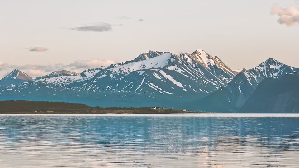 A mountain range with snow-capped peaks and a calm lake in the foreground.