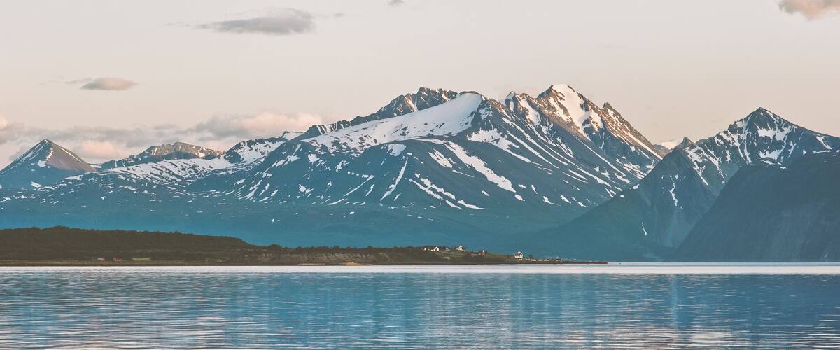 A mountain range with snow-capped peaks and a calm lake in the foreground.