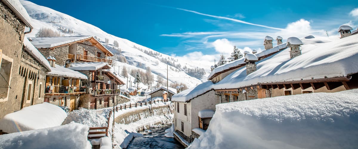 Un pueblo nevado en la montaña con casas de madera y un arroyo estrecho lleno de nieve.