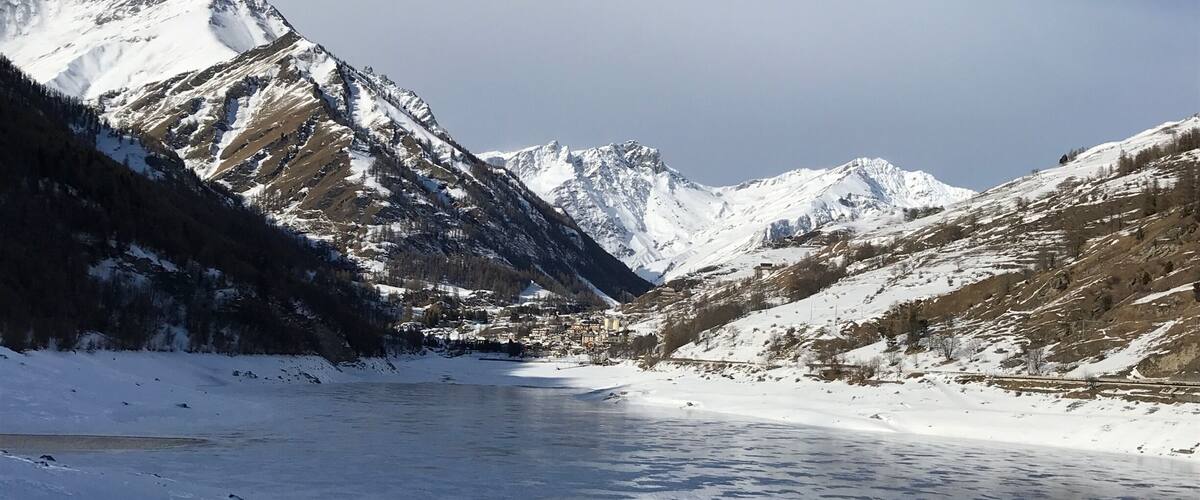 A snow-covered valley with a frozen river and mountains in the background.